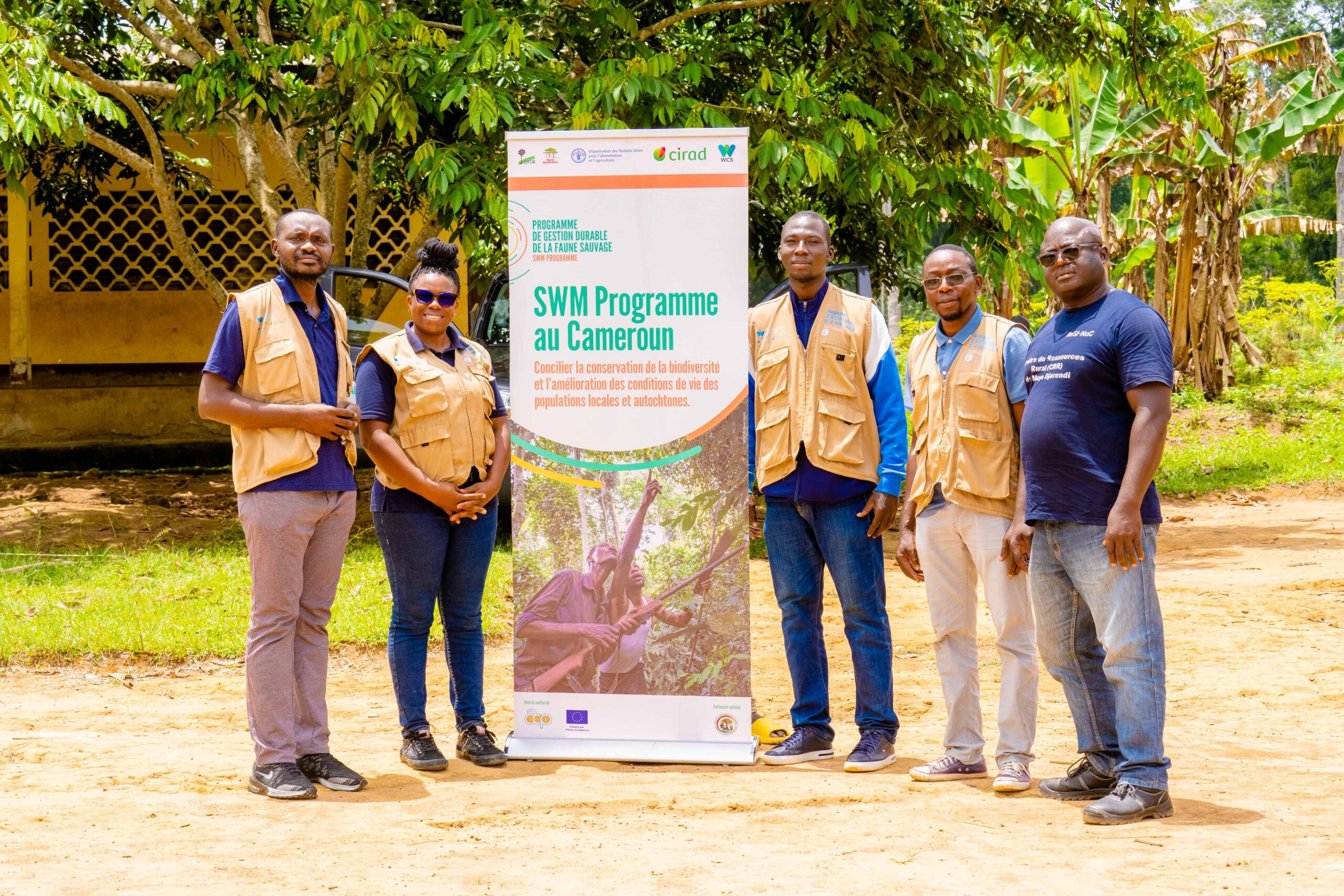 SWM Programme staff and partners standing beside a project banner in southern Cameroon