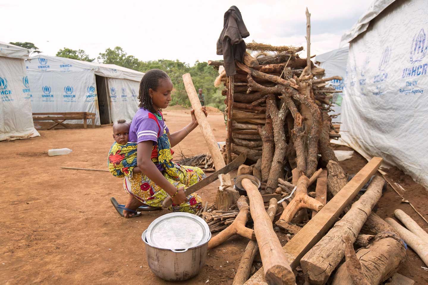 Une réfugiée du camp de réfugiés de Ngam porte son bébé pendant qu'elle coupe du bois avec une machette. Photo : ONU Femmes/Ryan Brown