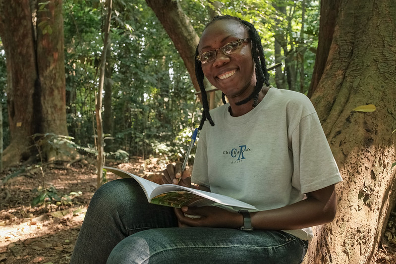 A student sits at the base of a tree with an open notebook