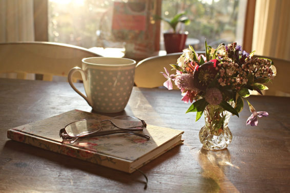 Tea cup, book, glasses and a small vase of flowers on a table