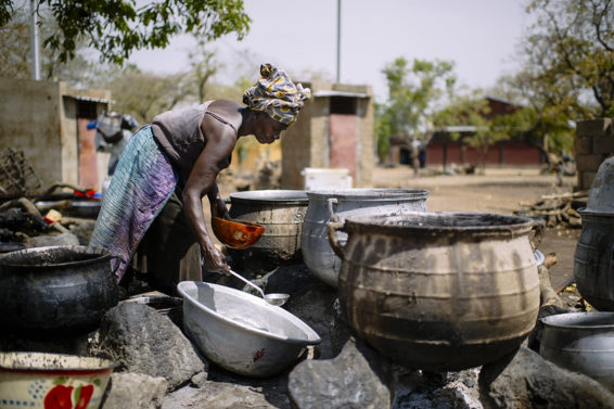 A woman surrounded by pots and cauldrons, processes shea