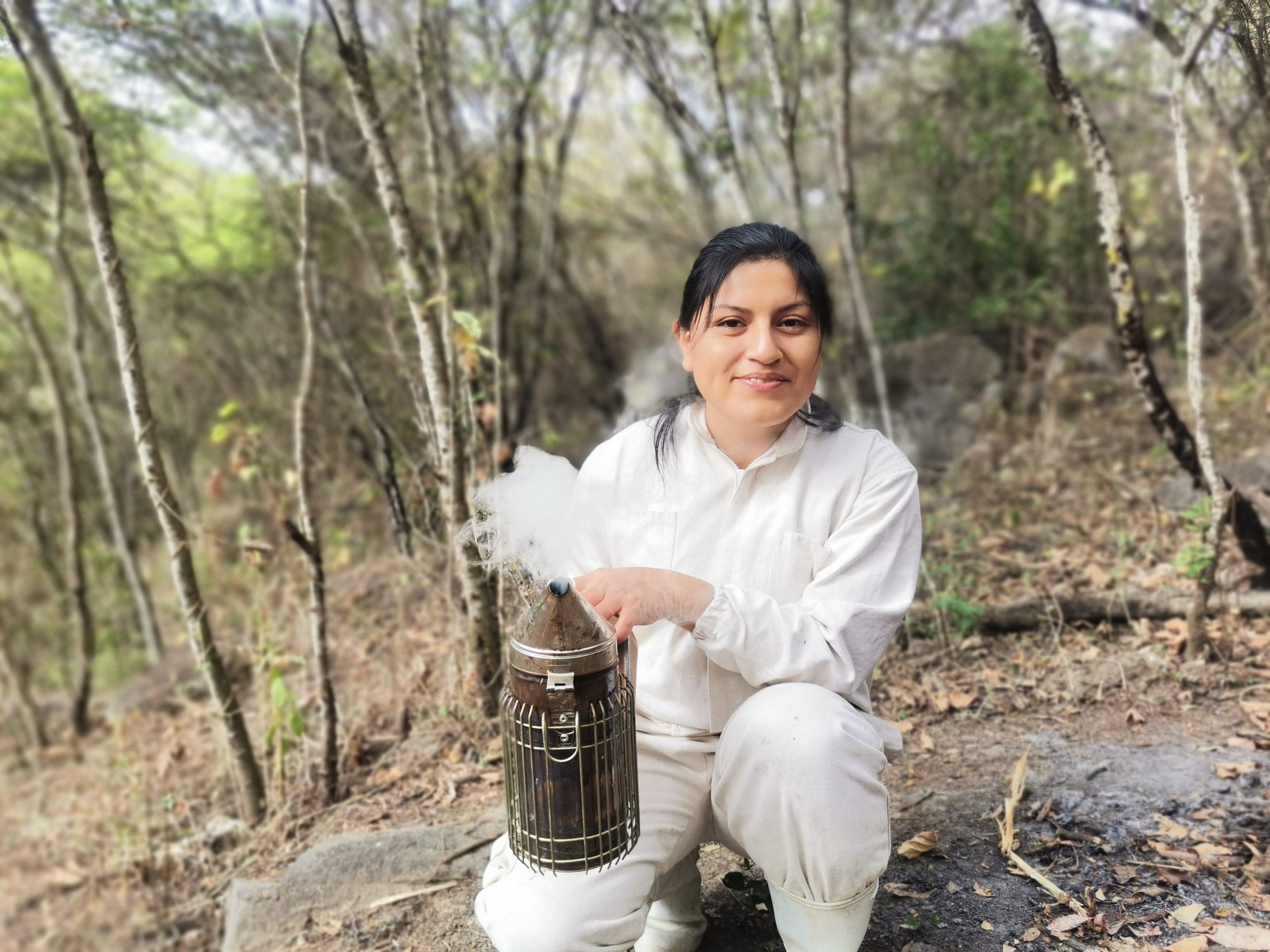 Ysabel Calderón kneels in a dry forest holding beekeeping equipment used to care for native stingless bees.