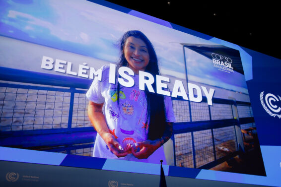 Smiling delegate standing by a riverside railing in front of a large “Belém is Ready” display at the Bonn Climate Change Conference, promoting Brazil’s upcoming COP30 in Belém, Amazon region.