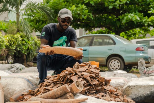Charles Emogor holding an elephant tusk next to a pile of pangolin scales confiscated by the Nigeria Customs Service in Nigeria, illustrating challenges to wild meat sustainability and wildlife conservation.