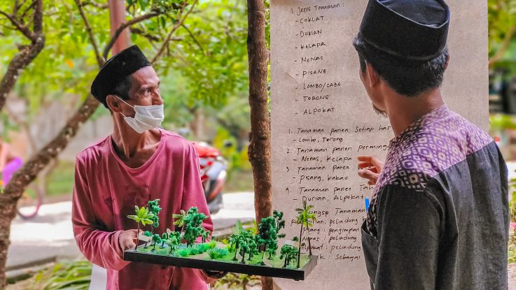 Farmer in North Luwu, Indonesia, holding an agroforestry model during a participatory training that helps design locally adapted land management systems.