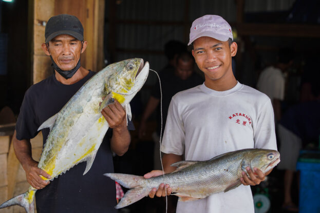 Two fishers hold large fish in Sungsang village, South Sumatra, Indonesia.