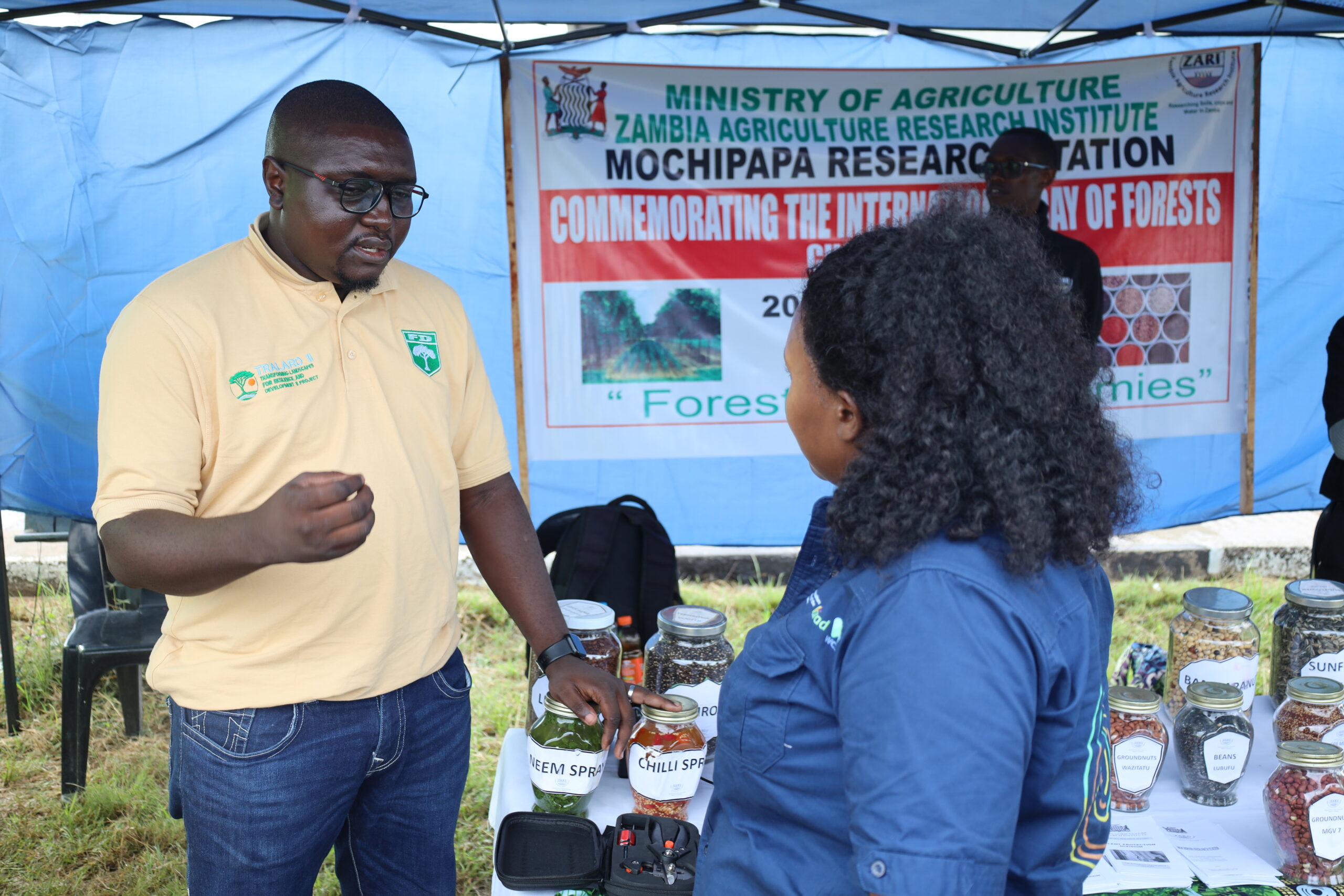 Yasa Luo Chisanga speaks with a visitor beside an exhibition display.