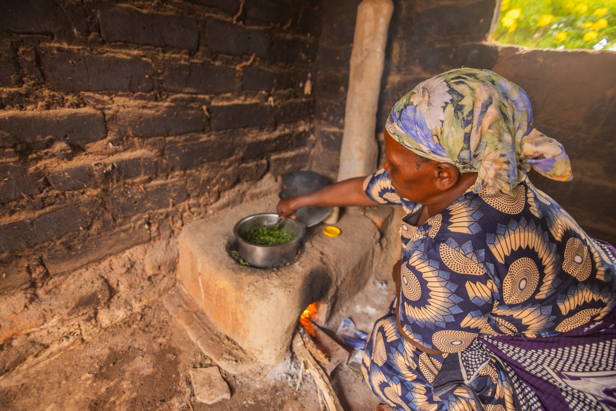 A woman tends a cooking pot on a wood-burning stove inside a rural home in Kenya.