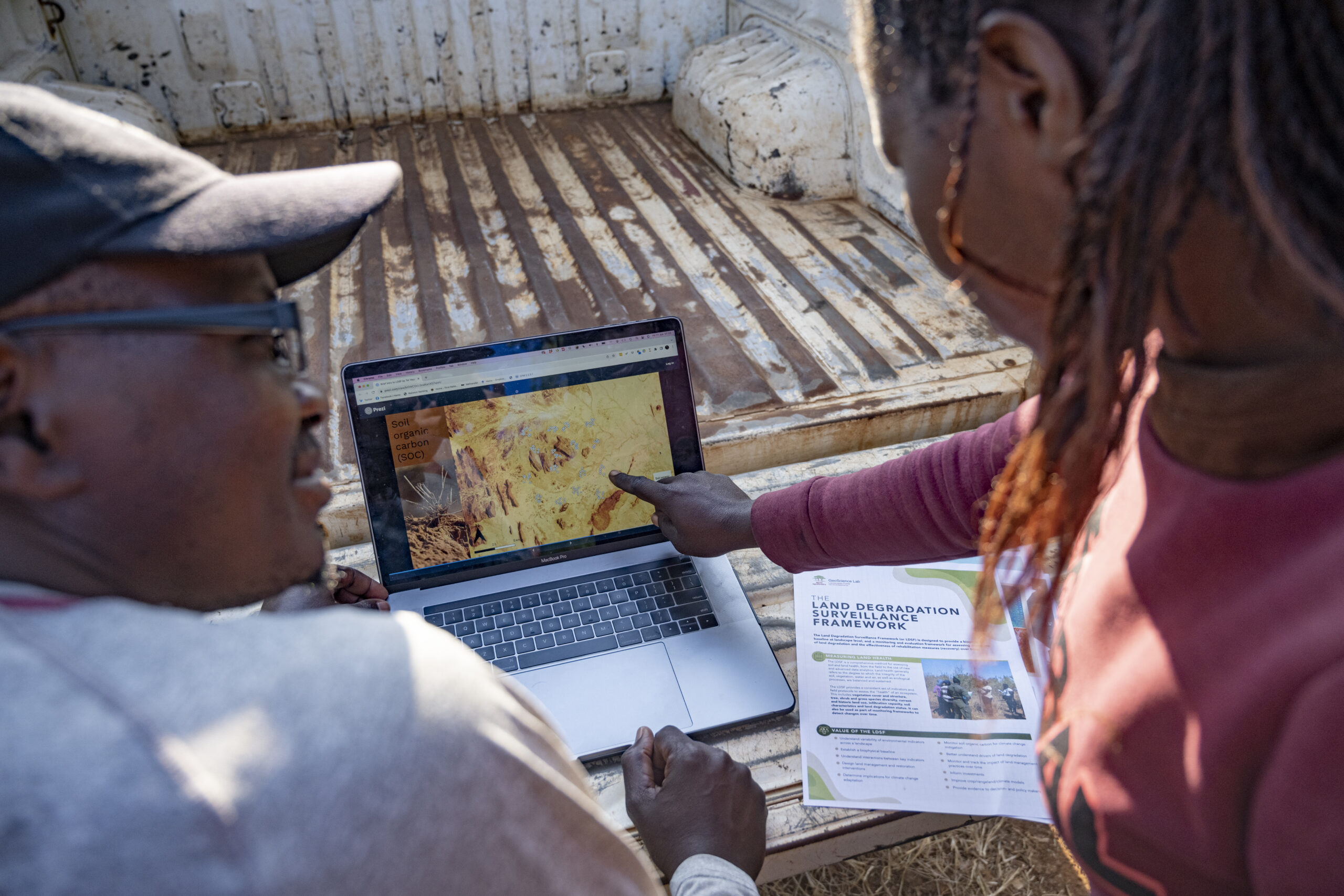 Two researchers review Land Degradation Surveillance Framework (LDSF) data on a laptop during fieldwork in Malawi, using digital maps to assess soil and land health.