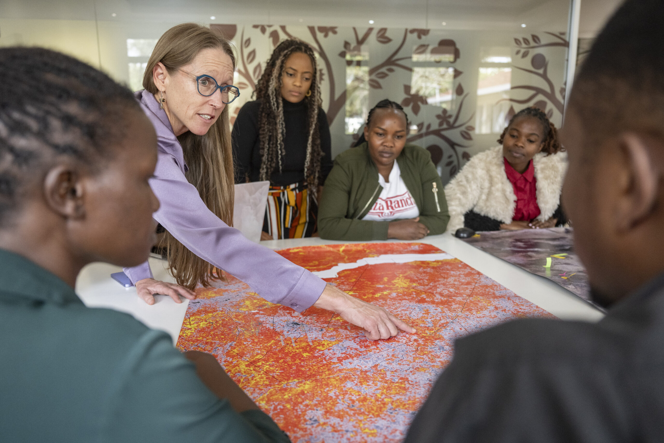 Leigh Ann Winowiecki points to a large landscape map while discussing restoration planning with colleagues.