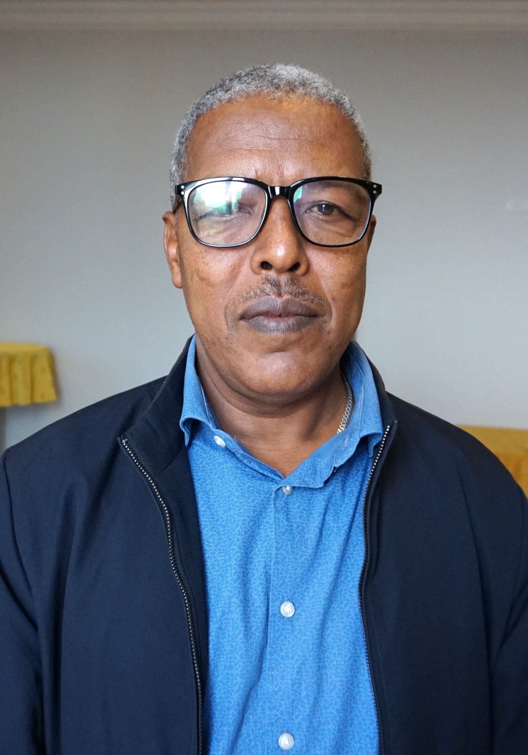 Portrait of Issme Lealem Mihret wearing glasses, a blue shirt and dark jacket.