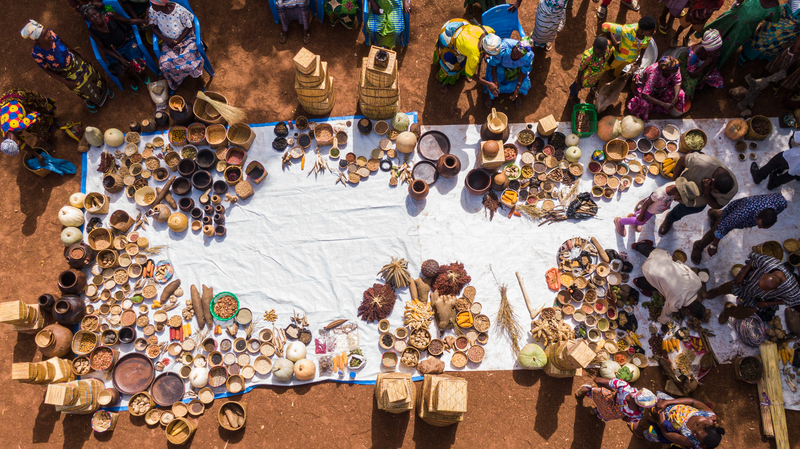 An overhead view of women displaying seeds, food products and handmade baskets and utensils at a market in Tachara.