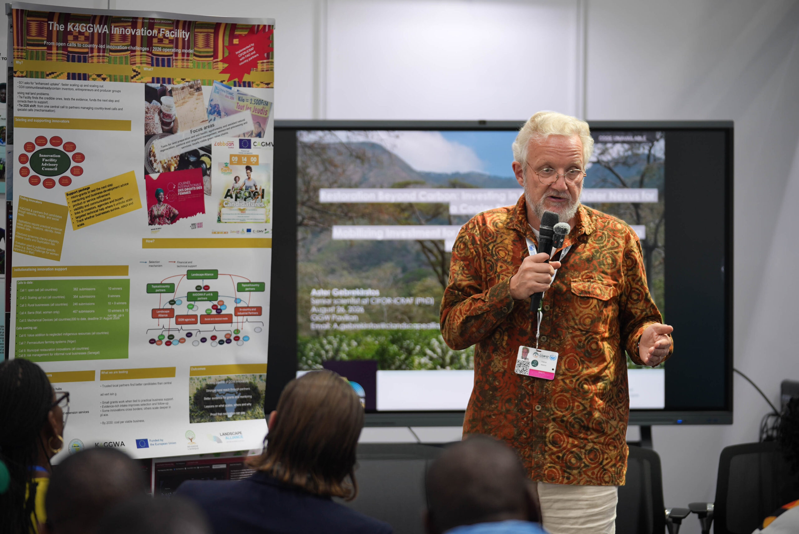 Patrick Worms speaks into a microphone during a session on financing the water-land nexus at UNCCD COP17, with K4GGWA materials displayed behind him.