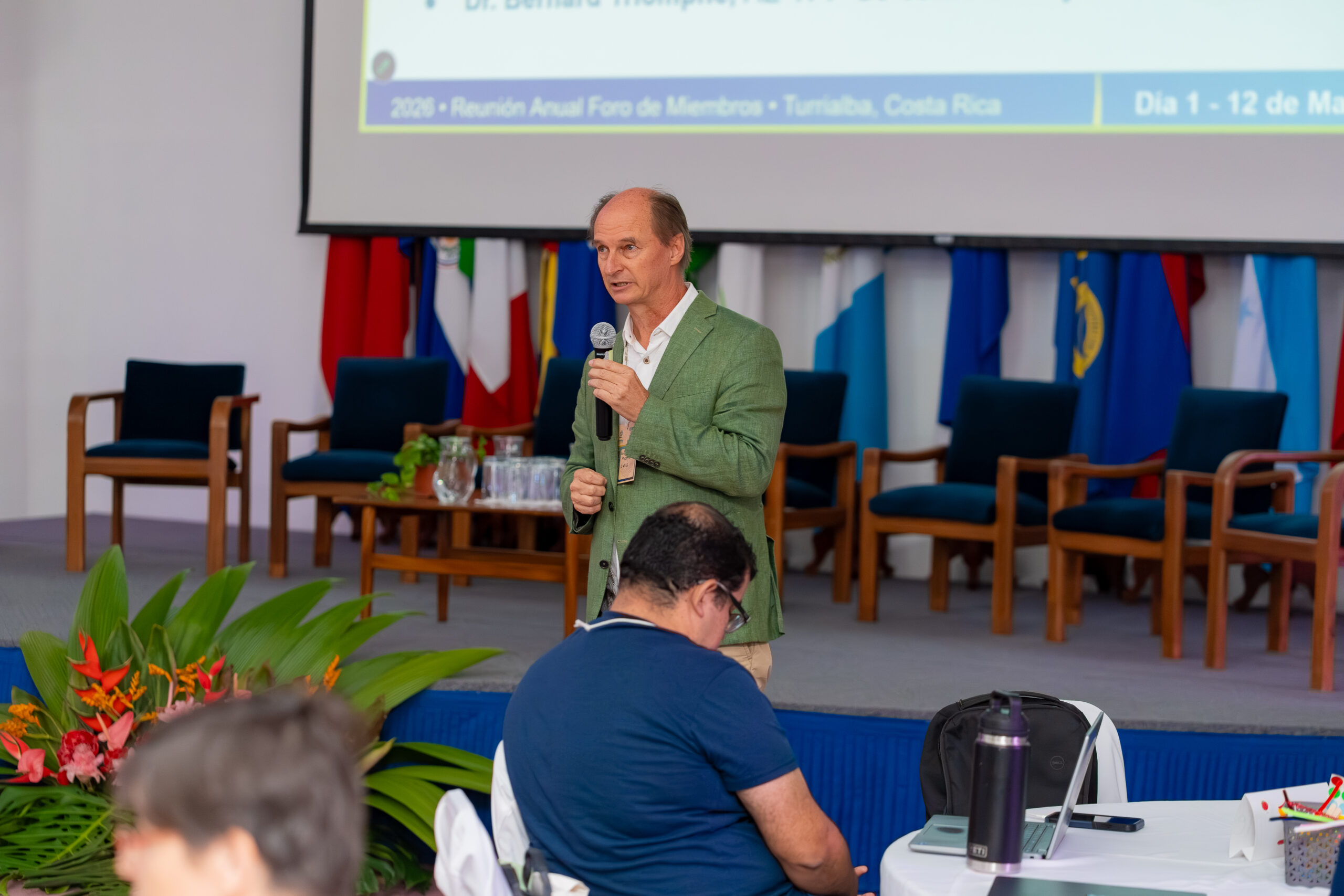 Reinhold Muschler speaks into a microphone in front of seated participants during the forum.