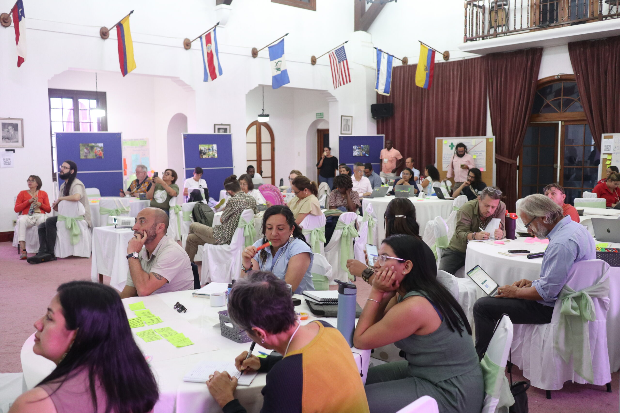 Forum participants sit around tables in a large meeting room, taking notes and working on group activities.