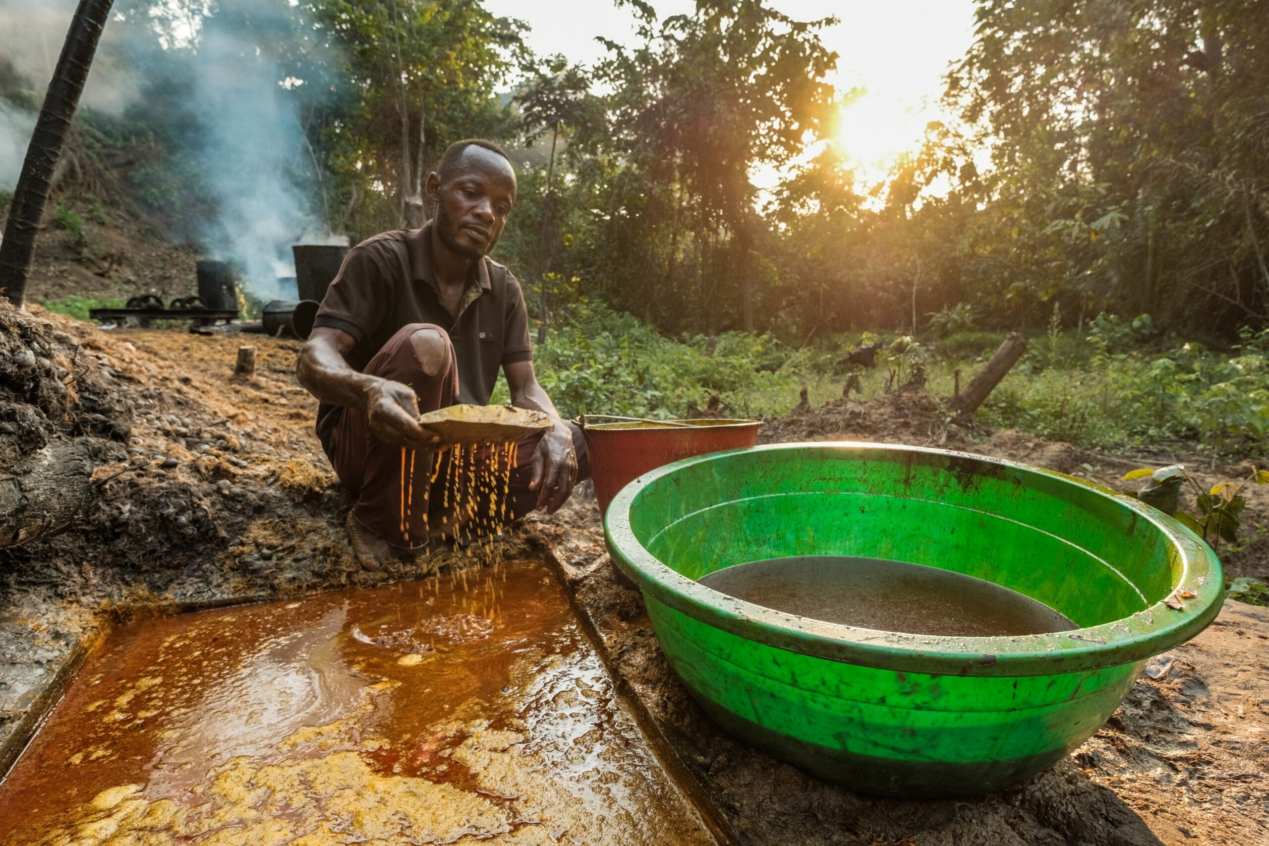 A person processing palm fruit beside a basin containing freshly extracted red palm oil.