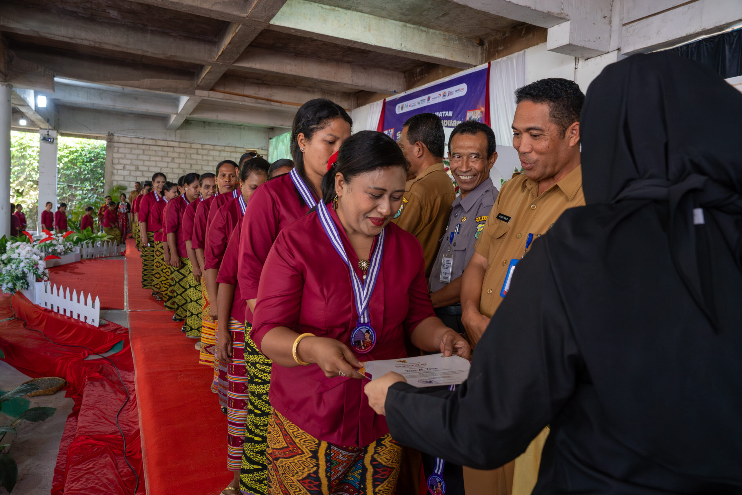 A woman receives her graduation certificate during a Skol Bife Women’s Field School ceremony in Timor, Indonesia, as other graduates wait in line.