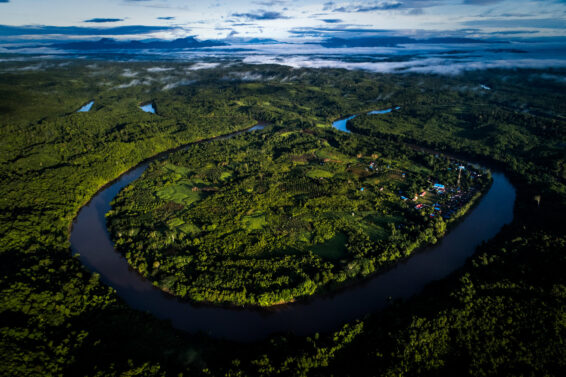 Aerial photograph of Buluq Sen village beside the Mahakam River in East Kalimantan, Indonesia, showing winding rivers, dense tropical forest and patches of farmland within a green landscape.