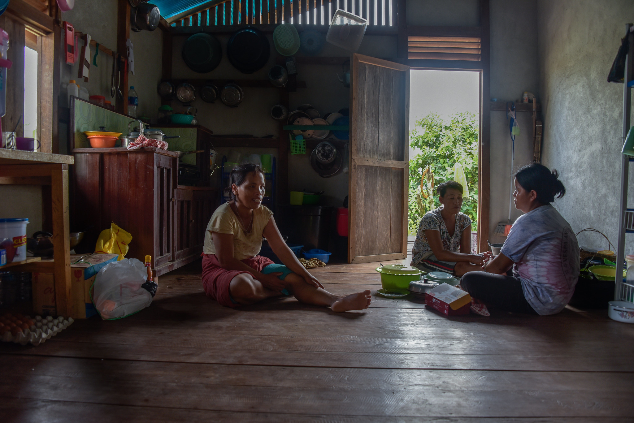 Three women sit and talk on the wooden floor of a modest kitchen in Central Kalimantan, Indonesia, reflecting the role of local communities in shaping fair and inclusive climate solutions.