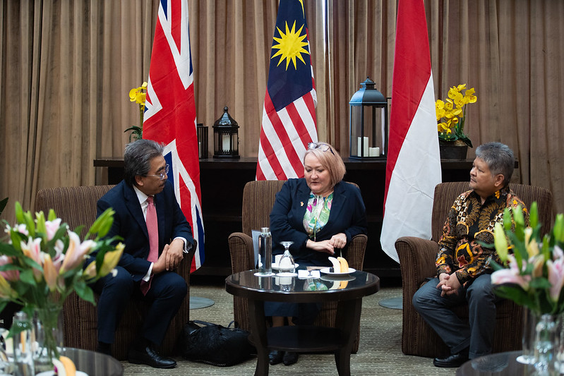 Three government representatives seated in discussion at the FACT Dialogue Forum 2025, with national flags displayed behind them.