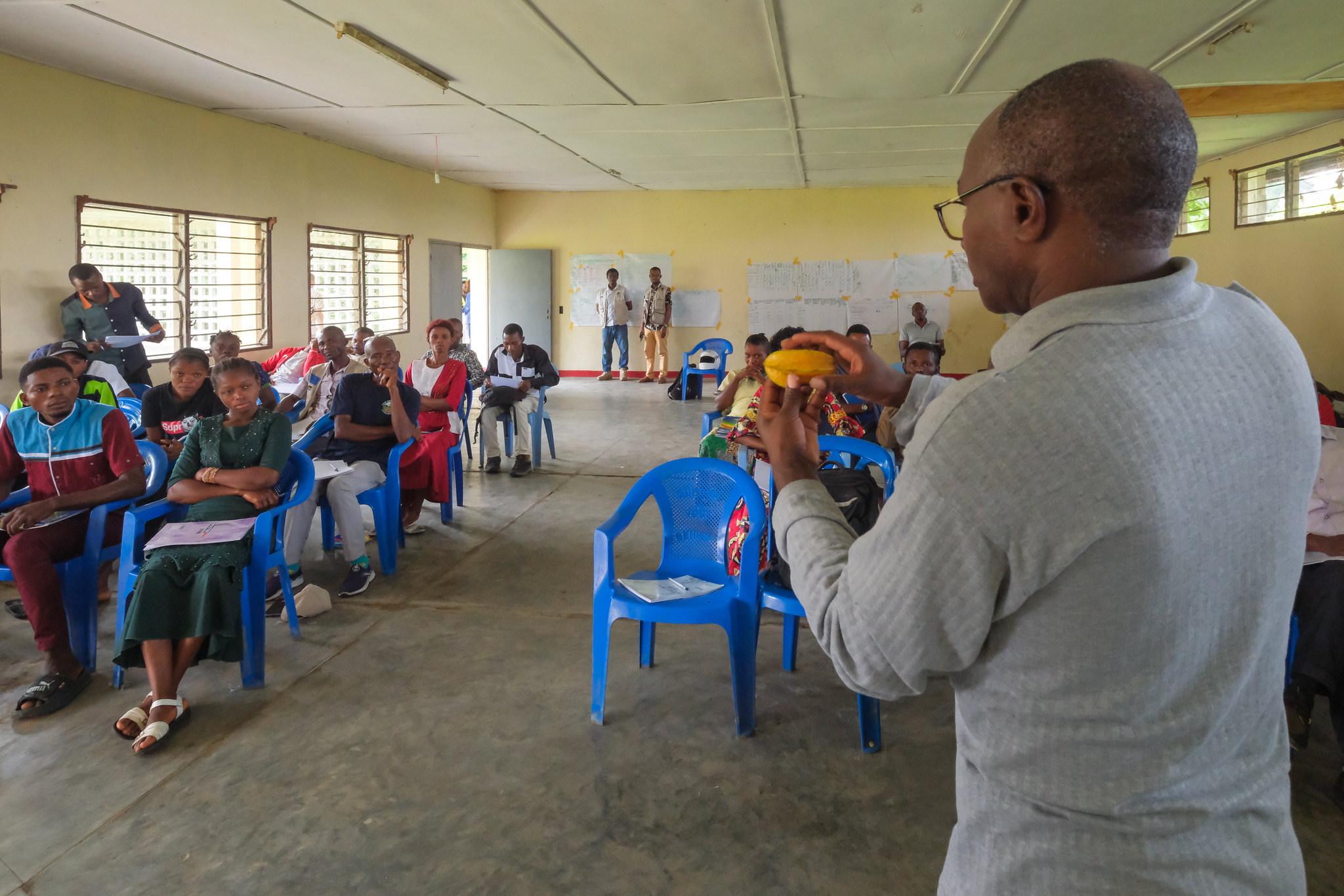 A facilitator speaks to farmers during a NutriScapes workshop in Yangambi, holding food items to discuss nutrition and livelihoods.