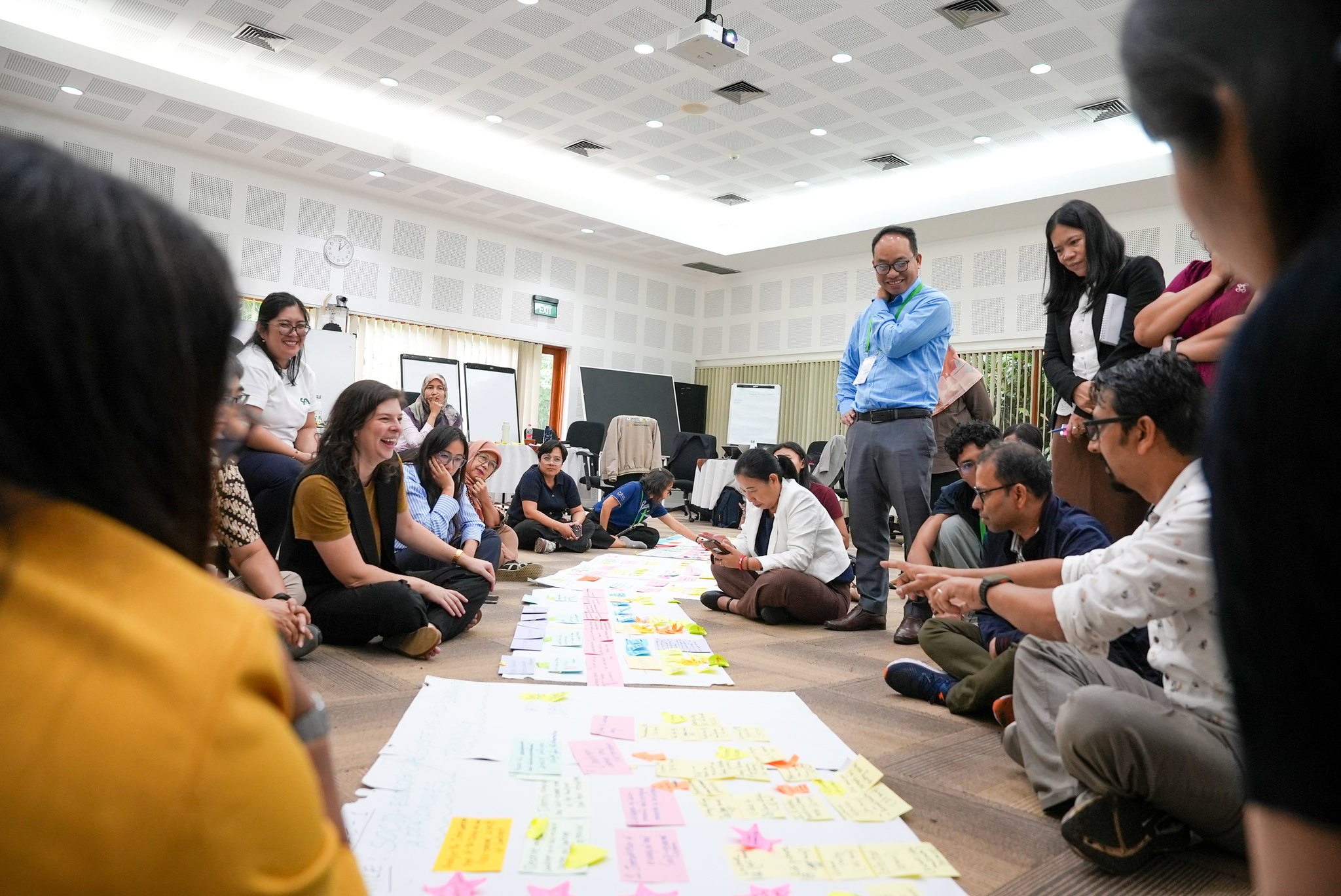 Participants sitting in a circle discussing and organising notes on large sheets of paper during a restoration education workshop at CIFOR-ICRAF Bogor campus.