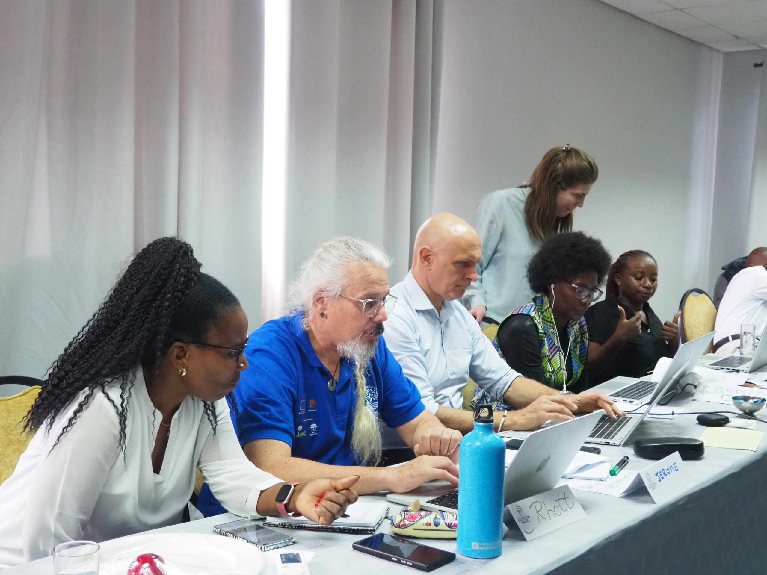 Participants seated at a table working on laptops and notes during a RAENS meeting session in Lusaka, Zambia.