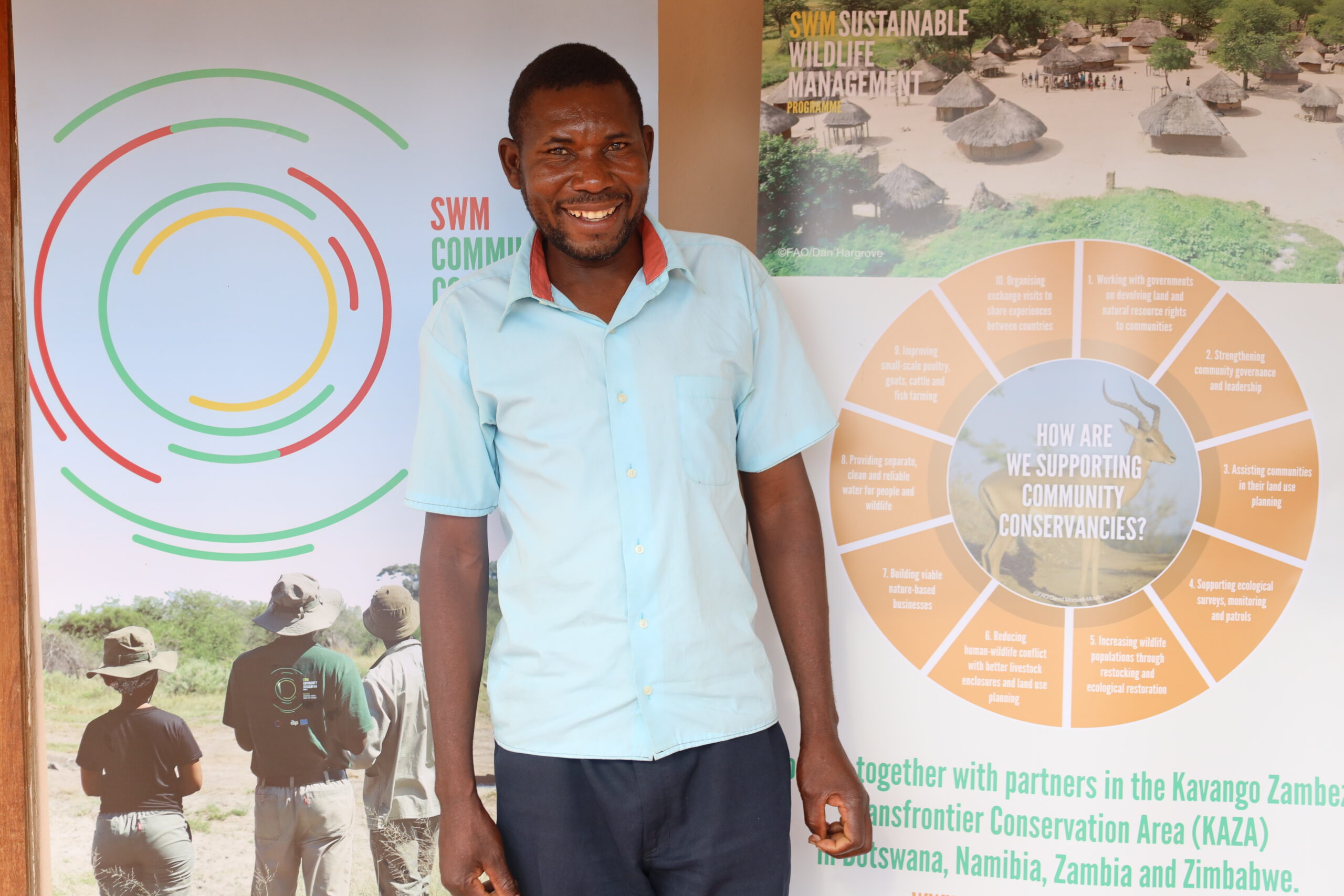Portrait of Elliot Mudenda standing in front of Sustainable Wildlife Management Programme posters.