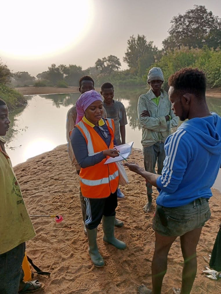 Sandra Owusu-Gwamfi reviewing field notes with local collaborators beside a river during amphibian research in West Africa.