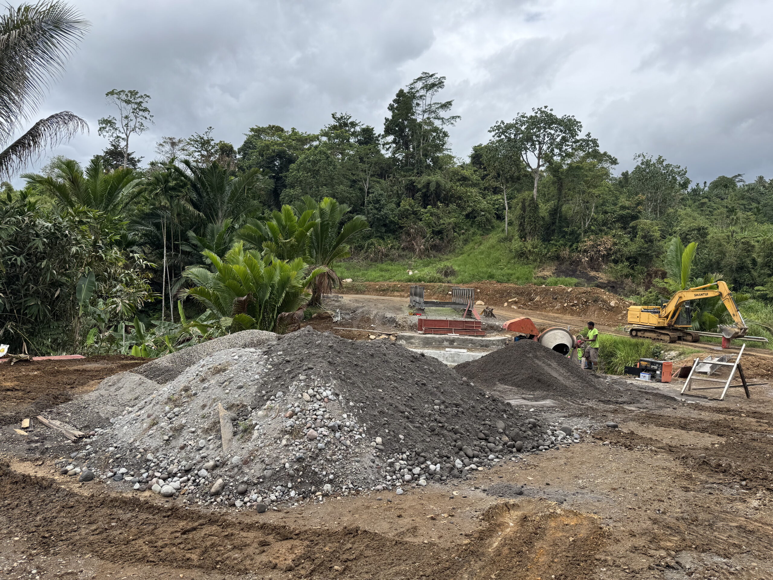 Workers and machinery repairing a damaged road bridge in a forested landscape.