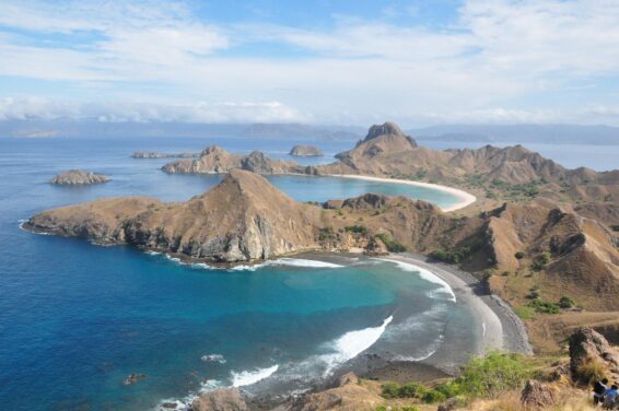 Dry, sparsely vegetated hills near Labuan Bajo, eastern Indonesia, showing degraded land with scattered trees and coastal waters in the background.